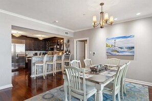 Un comedor con una mesa y sillas, un candelabro, un cuadro y una cocina al fondo.