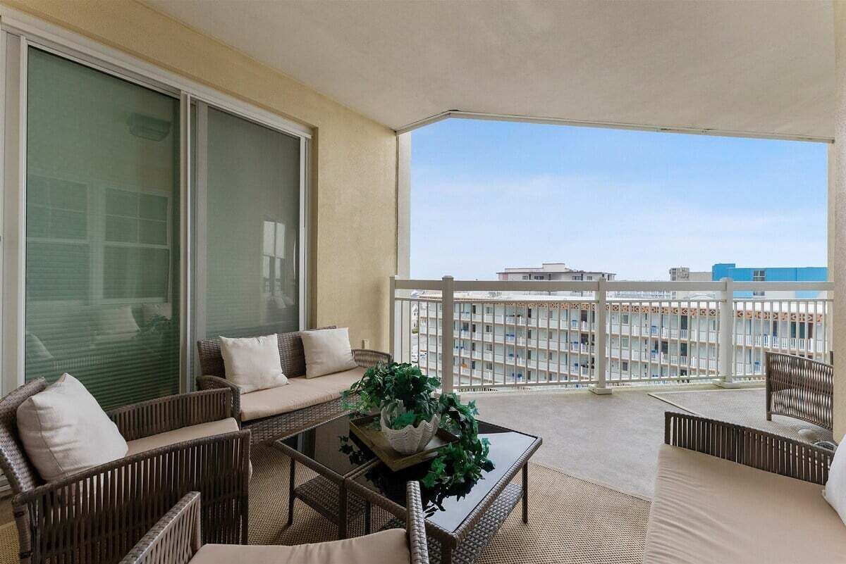 Ein Balkon mit Korbmöbeln, einem Glastisch und einem Blumentopf.