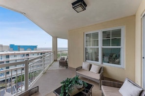 A balcony with a sofa, a table with a plant, and a large window. - Residence 509 at The Grand (Wildwood)