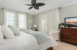 Quarto com cama, televisão, cômoda, cadeira e ventilador de teto.