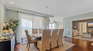 Uma sala de jantar com mesa, cadeiras, uma planta e vista para o exterior.