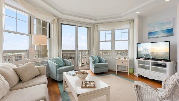 A spacious living room with a large window, a flat-screen TV, and a comfortable seating area. - Residence 703 at The Grand (Wildwood)