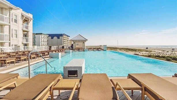 Ein Poolbereich mit Liegestühlen, einem Rettungsturm und Blick auf den Strand.