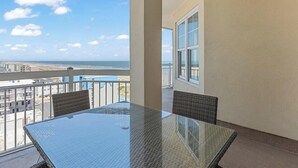 Ein Balkon mit Glastisch und Stühlen, der auf einen Strand und eine Stadtansicht blickt.