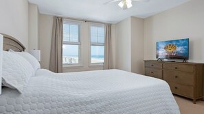 A hotel room with a large bed, a television, a dresser, and a window with curtains.