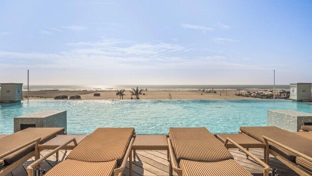 A pool with lounge chairs, a view of the beach, and a clear sky. - Residence 308 at The Grand (Wildwood)