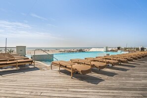 Een houten terras met lounge stoelen en een zwembad.