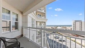 Een balkon met uitzicht op het strand en de parkeerplaats.