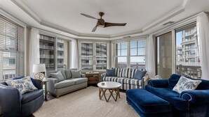 A living room with a ceiling fan, a sofa, a striped couch, and a blue armchair. - Residence 102 at The Grand (Wildwood)
