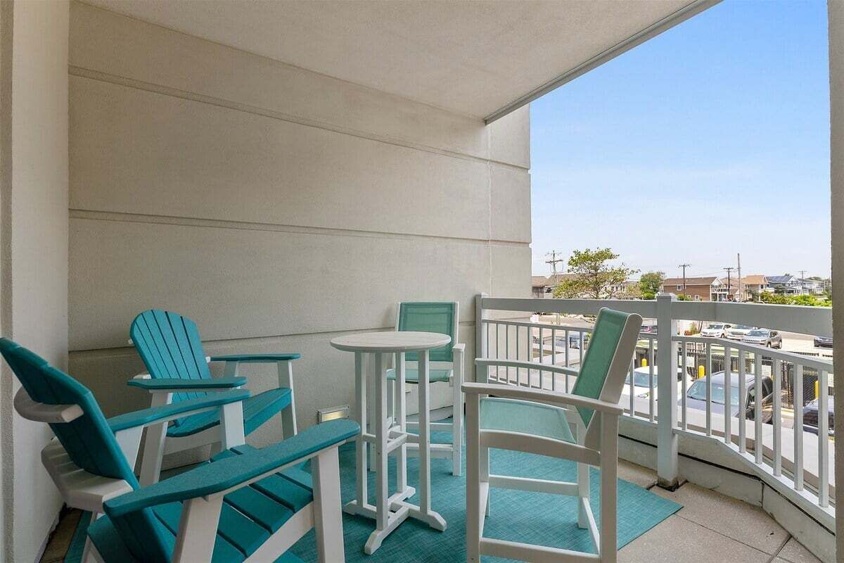 Een balkon met stoelen en een tafel, met uitzicht op een straat met geparkeerde auto's en gebouwen.