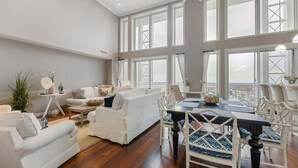 Un vaste espace de vie comprenant une grande table à manger, des meubles blancs et de grandes fenêtres offrant une vue dégagée.
