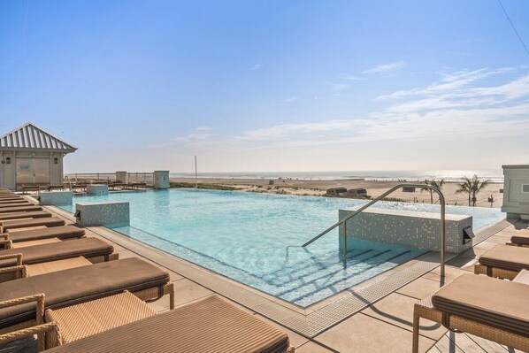 A pool area with lounge chairs and a view of the beach.