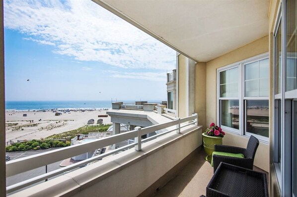 Un balcon avec vue sur la plage et l’océan, une plante en pot et une chaise en osier.