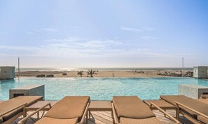Une piscine avec des chaises longues, une vue sur la plage et un ciel dégagé.