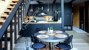 Een moderne keuken met een centraal eiland, houten balken en een trap naar een hoger niveau.