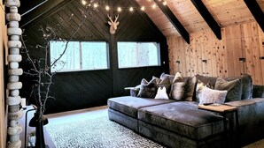 Een knus loft slaapkamer met een donker houten plafond, een zachte grijze bank met veel kussens, en een lichtslingering.