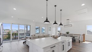 A spacious kitchen with a large island, white cabinetry, and pendant lighting. - Carolina Blue Skies is 2nd Row, Steps to the Beach, Ocean Views and New Construction (Holden Beach)