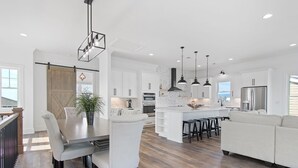 A modern kitchen with white cabinetry, a central island, pendant lighting, and a view to the outside. - Carolina Blue Skies is 2nd Row, Steps to the Beach, Ocean Views and New Construction (Holden Beach)
