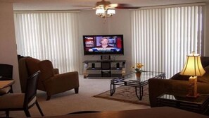 Una sala de estar con una televisión, dos sillones, una mesa de centro y una lámpara.