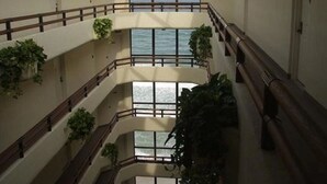 Un interior de varios niveles con balcones, ventanas amplias y plantas en macetas.