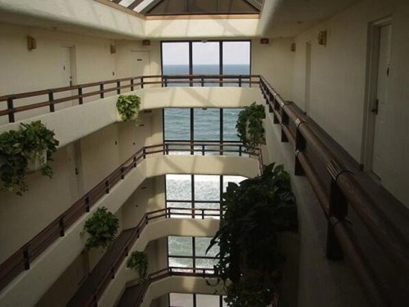 Un interior de varios niveles con balcones, ventanas amplias y plantas en macetas.