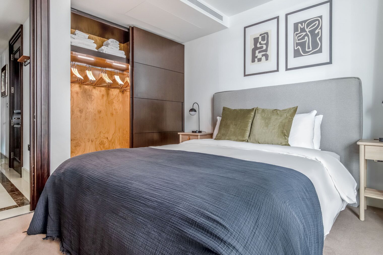 Une chambre d’hôtel avec un grand lit, une armoire en bois, une table de chevet et deux tableaux encadrés au mur.