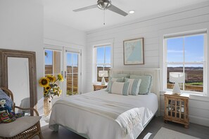 Une chambre dotée d’un grand lit, d’un ventilateur de plafond et offrant une vue sur le paysage par les fenêtres.