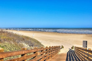 A wooden boardwalk leading to a sandy beach with the ocean in the background.