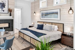 Une chambre à coucher moderne, avec un lit, des tables de chevet, une petite table avec des chaises, une cheminée et des œuvres d’art accrochées aux murs.