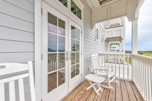 A covered porch with white railings, a wooden deck, and a view of the ocean.