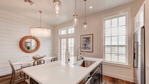 A kitchen with a large island, stainless steel appliances, and a view through the window. - Rooftop Balcony, Boardwalk to Beach, Resort Pool (Port Aransas)