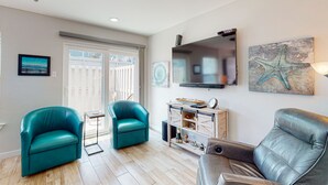 Ein Wohnzimmer mit türkisfarbenen und schwarzen Ledersofas, einem kleinen Beistelltisch, einer weißen Kommode mit Dekorationen und einem Kunstwerk mit Seestern an der Wand.