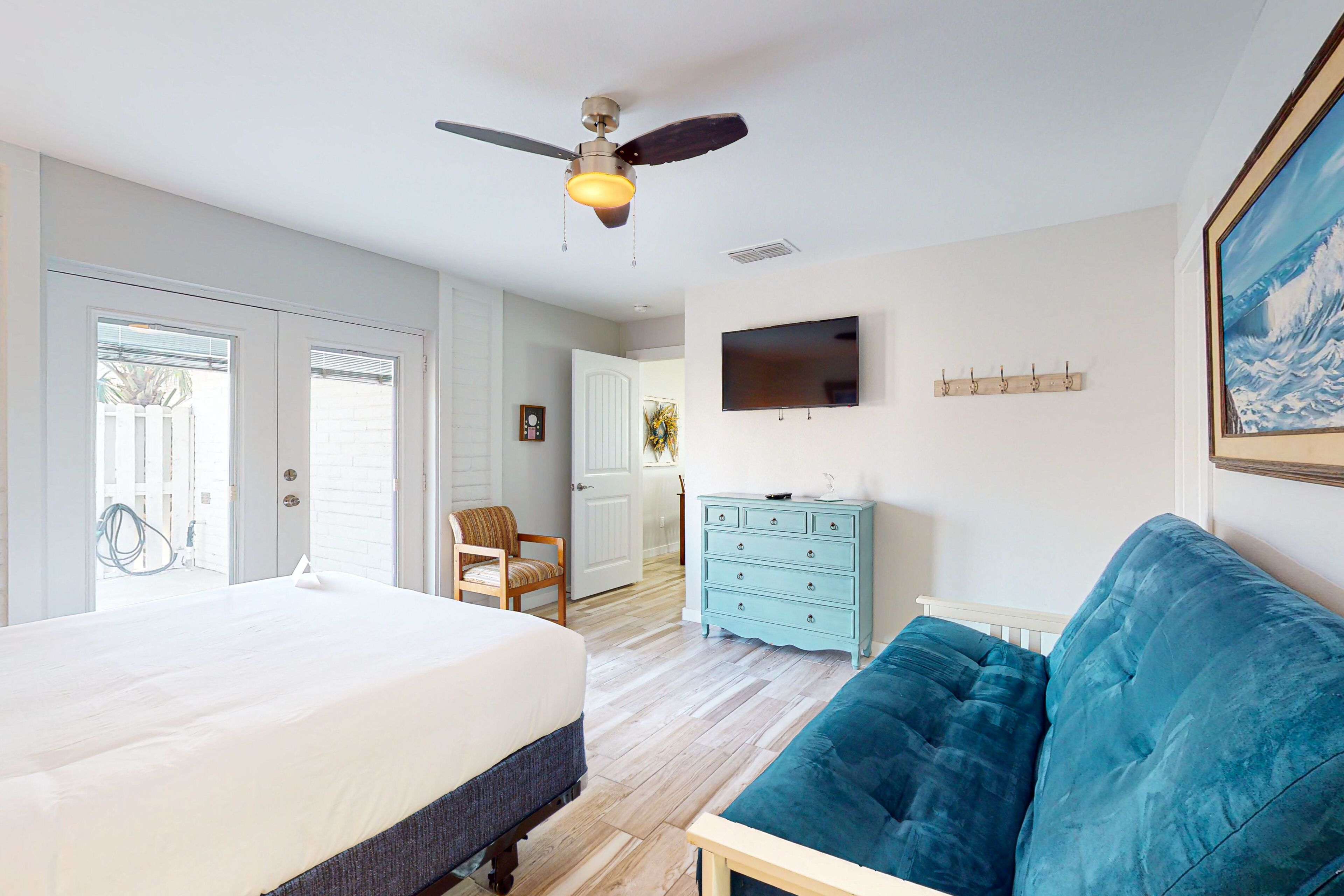 A bedroom with a bed, a blue sofa, a ceiling fan, a dresser, and a television on the wall.