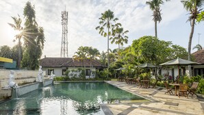 A swimming pool with statues, palm trees, and outdoor seating. - Jimbarwana Hotel (Negara)