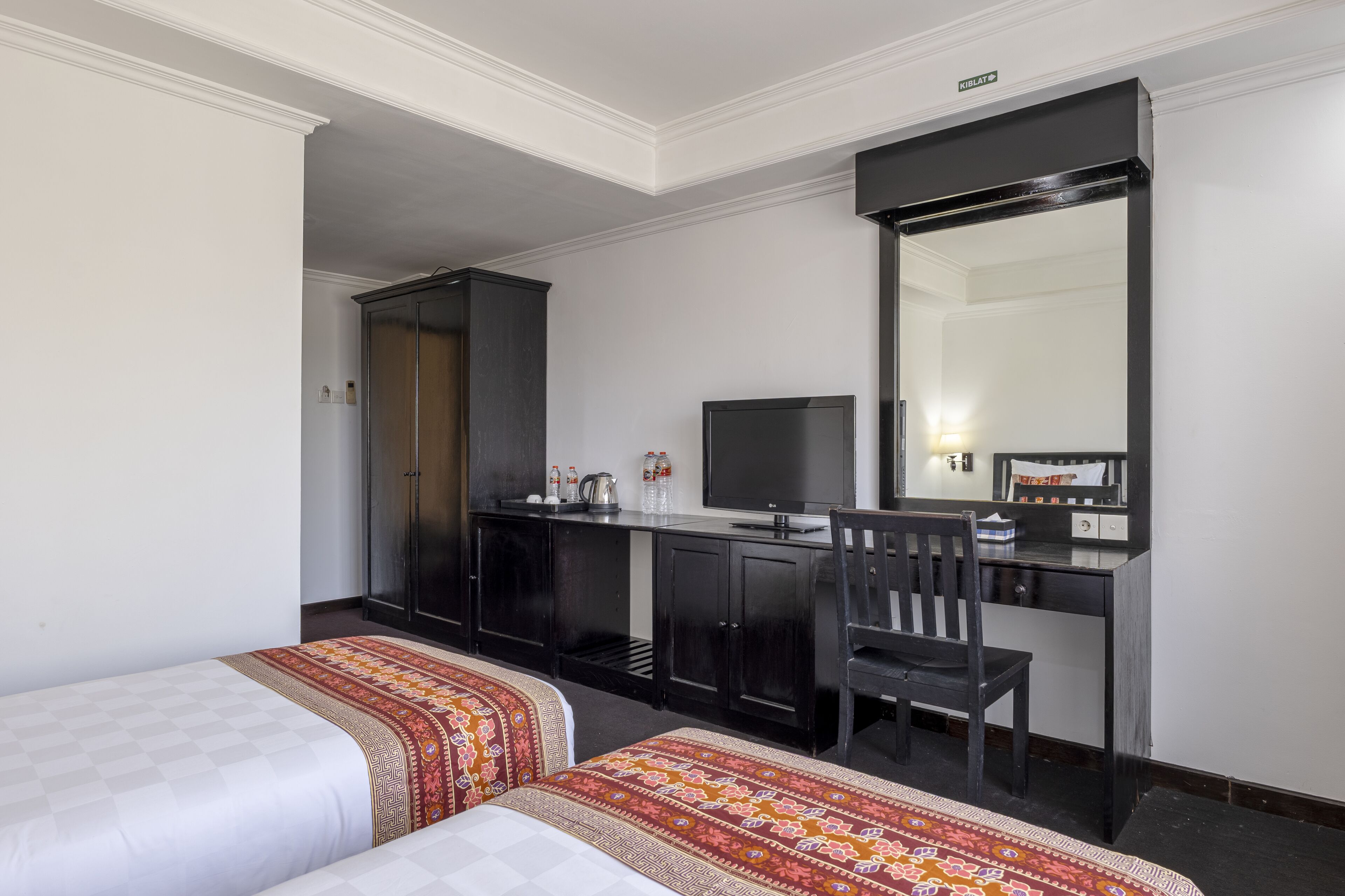 A hotel room with two beds, a desk with a chair, a television, and a wardrobe.