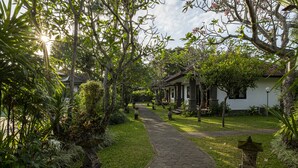 A garden pathway leading to a traditional house with a tiled roof, surrounded by lush greenery and stone lanterns. - Jimbarwana Hotel (Negara)