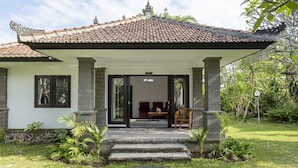A traditional house with a tiled roof, a covered porch, and a garden with various plants. - Jimbarwana Hotel (Negara)