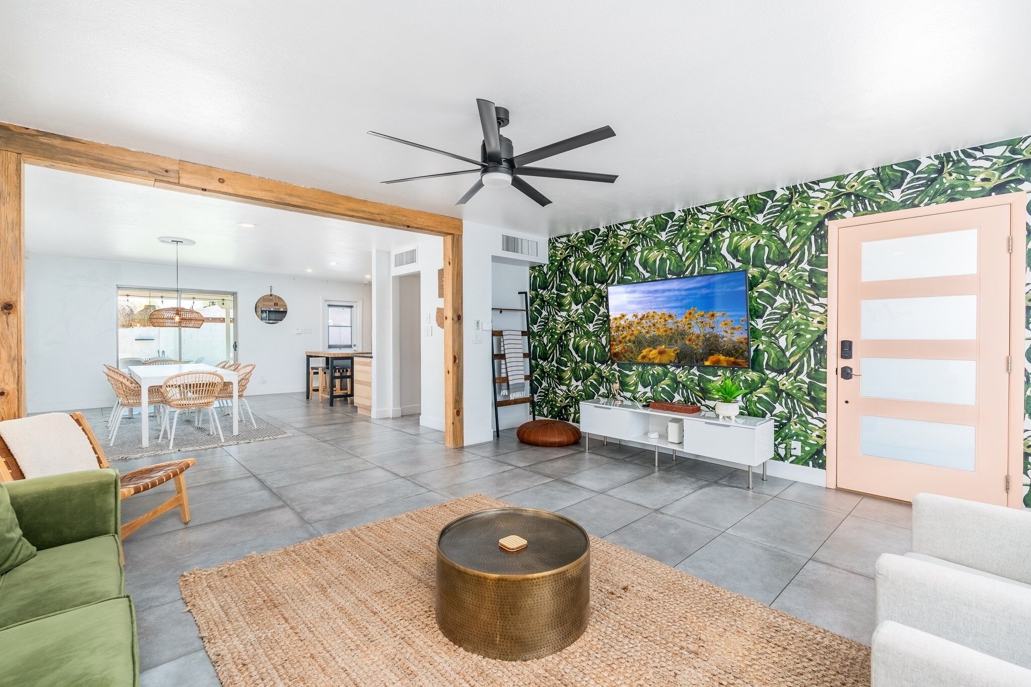 A modern living room with a large TV, a ceiling fan, and a wall with a tropical leaf pattern.