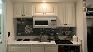 Une cuisine avec des meubles blancs, un four à micro-ondes et un dosseret carrelé.