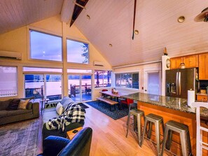 Un amplio salón con un ventanal que da a una terraza, una cocina equipada con nevera, y una zona de estar con sofá y sillones.
