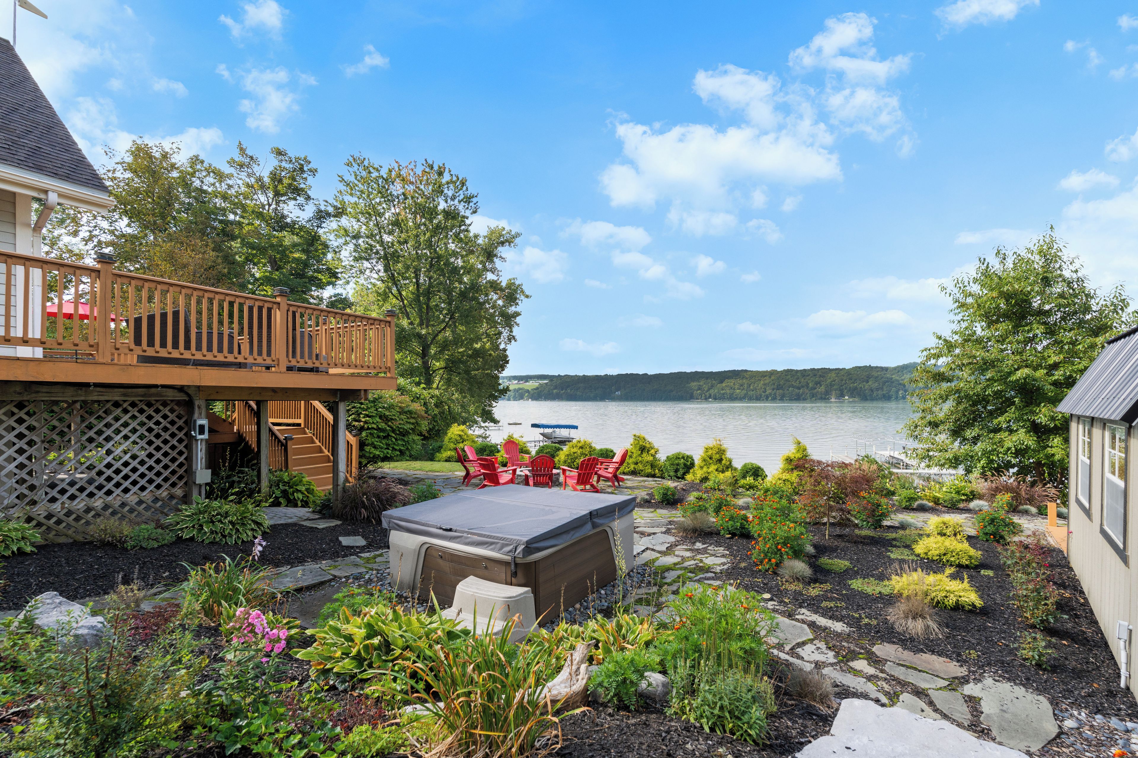 A deck with a view of a lake, surrounded by a garden with various plants and a hot tub.