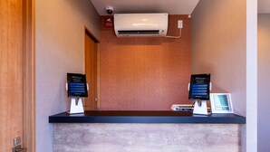 Un comptoir d’accueil avec deux bornes numériques, un appareil de climatisation au-dessus et une porte en bois sur la gauche.