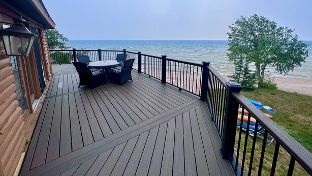 Une terrasse en bois avec une table et des chaises, donnant sur une plage et l’océan.