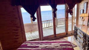 Une chambre avec un grand lit, un plancher en bois, une vue sur l’océan par une porte coulissante et une terrasse en bois à l’extérieur.