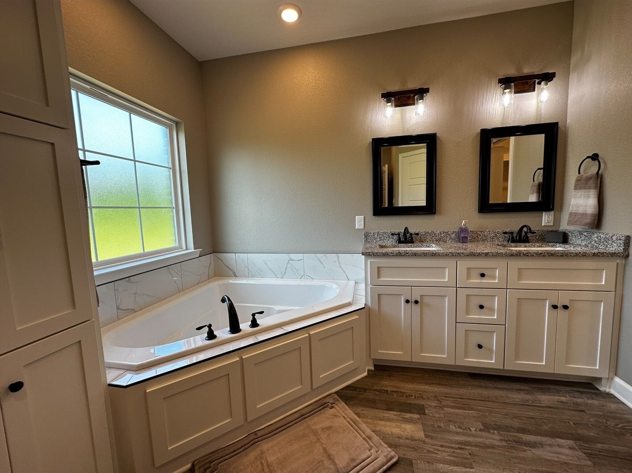 A bathroom with a large bathtub, a double vanity with two sinks, and a window providing natural light.