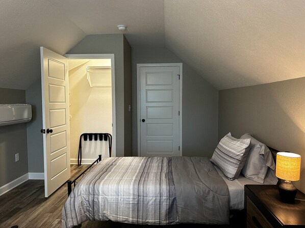 Un dormitorio con una cama, una mesita de noche con lámpara, un radiador y dos puertas.
