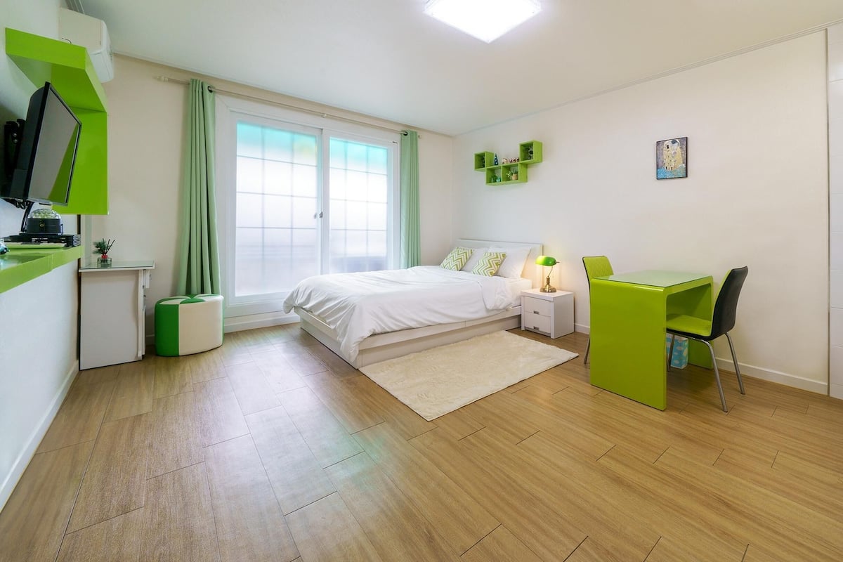 A modern, well-lit bedroom with a bed, bedside table, and a desk with a chair.