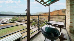 Un balcón con una parrilla, bancos de madera y vistas a un paisaje montañoso.