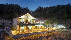 A two-story building with a balcony and a covered outdoor seating area, surrounded by trees and a stone wall. - Gapyeong Oneul-yeogipension (Gapyeong)