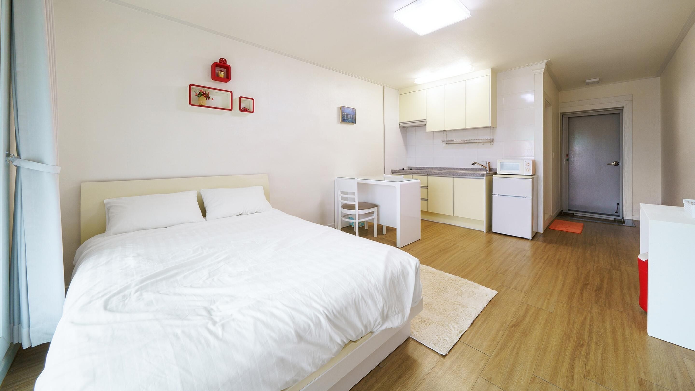 A bedroom with a bed, a desk, and a kitchenette.